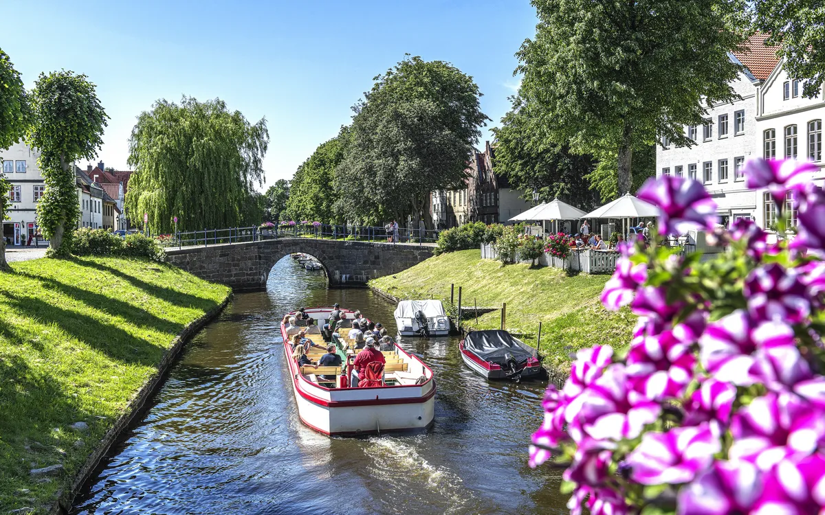 Boot auf einem Kanal in einer grünen Parklandschaft mit Brücke und Blumen im Vordergrund
