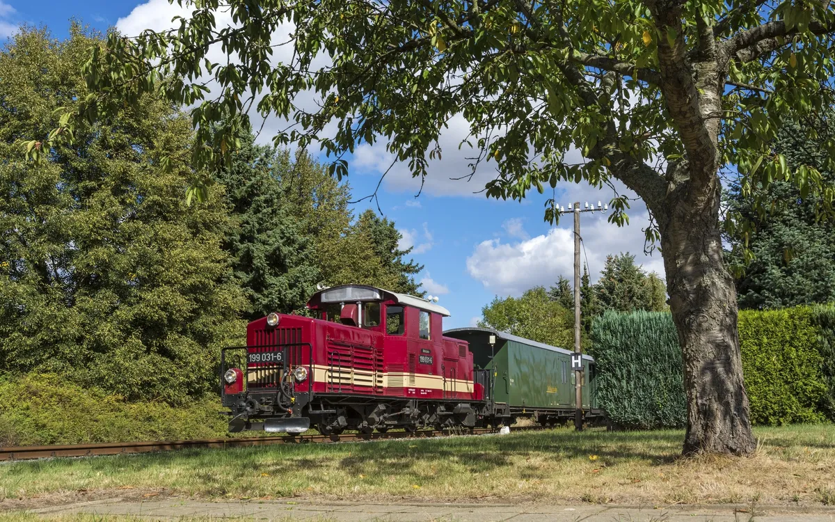 Rote Doellnitzbahn-Lok fährt durch grüne Landschaft bei sonnigem Wetter.