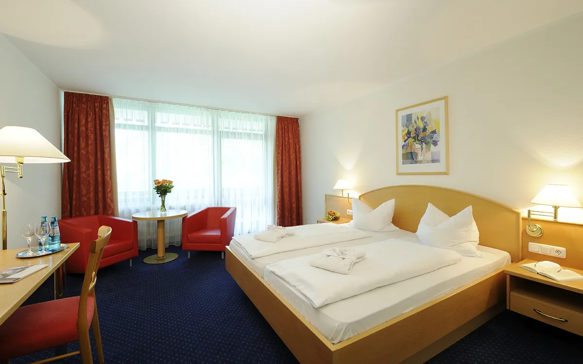 Helles Hotelzimmer mit Doppelbett, rotem Sessel und großem Fenster.