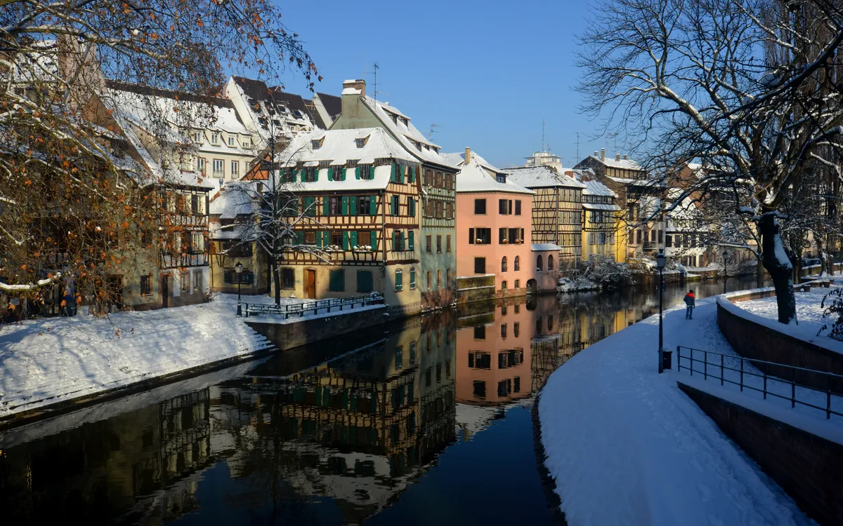 winterliches Straßburg im Elsass, verschneite Häuser, blauer Himmel und ruhiger Fluss