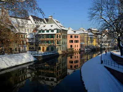 winterliches Straßburg im Elsass, verschneite Häuser, blauer Himmel und ruhiger Fluss