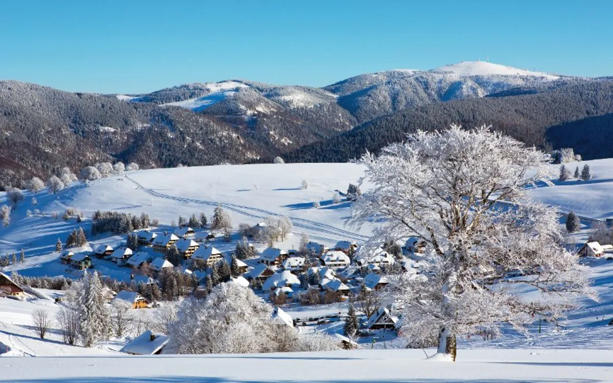 Verschneite Landschaft mit Dorf und Hügeln im Hintergrund.