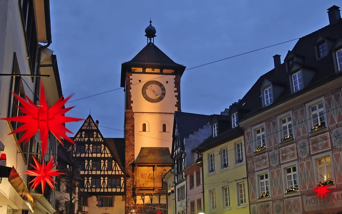 Historischer Uhrturm und Fachwerkhäuser bei Abenddämmerung, dekoriert mit Weihnachtssternen.