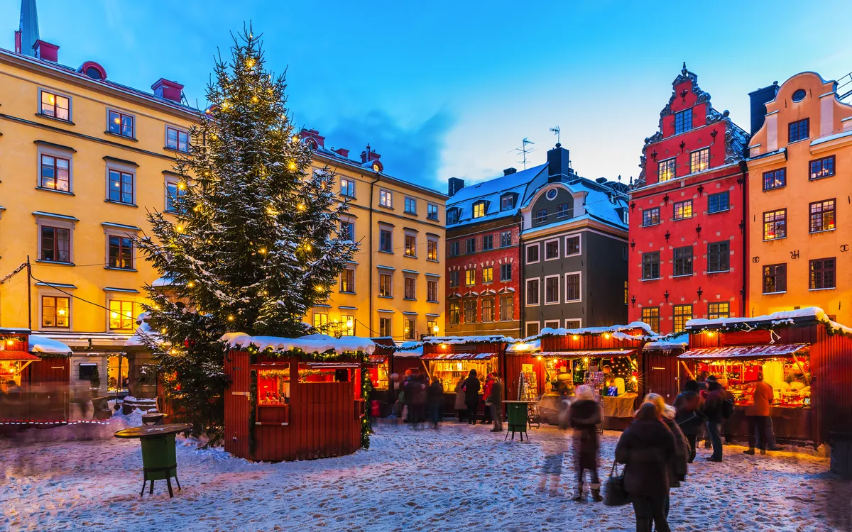 Weihnachtsmarkt auf einem verschneiten Platz mit geschmücktem Tannenbaum in der Abenddämmerung