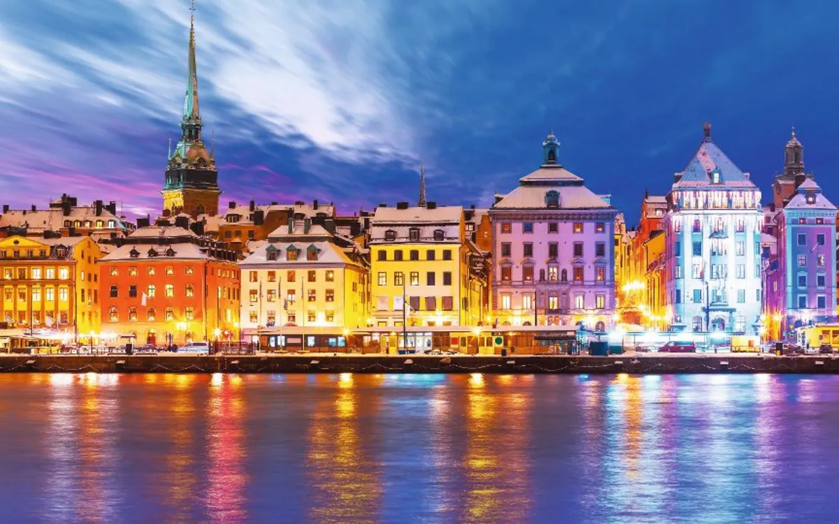 Bunt beleuchtete Stadtansicht bei Nacht mit Fluss im Vordergrund.