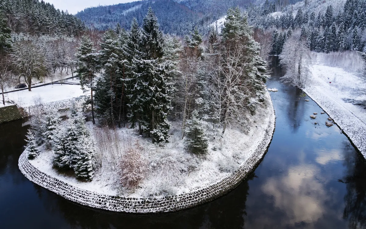 Verschneite Insel mit Bäumen, von einem Fluss umgeben.