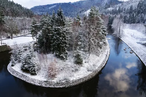 Verschneite Insel mit Bäumen, von einem Fluss umgeben.