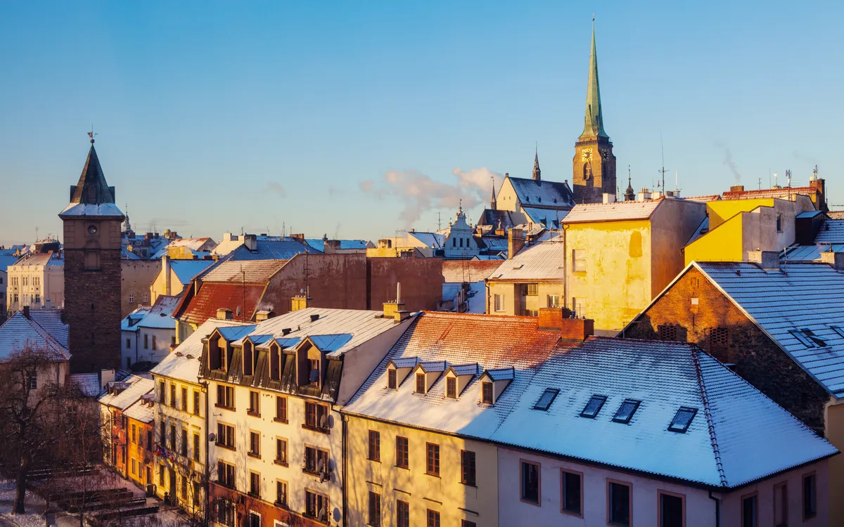 Verschneite Altstadt mit bunten Dächern und Kirchturm im Hintergrund bei klarem Himmel.