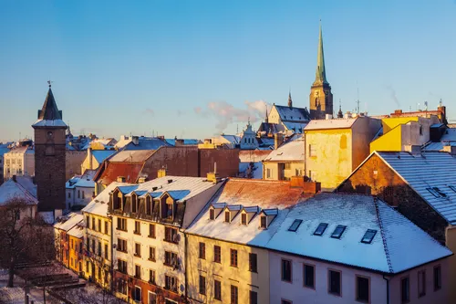 Verschneite Altstadt mit bunten Dächern und Kirchturm im Hintergrund bei klarem Himmel.