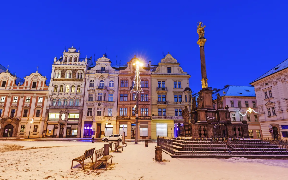Verschneiter europäischer Platz mit historischen Gebäuden und Statue bei Dämmerung.