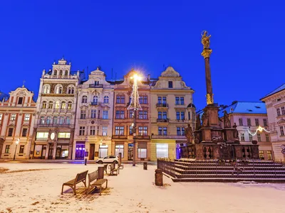 Verschneiter europäischer Platz mit historischen Gebäuden und Statue bei Dämmerung.