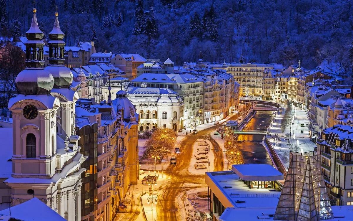 Winterliche Stadtansicht von Karlovy Vary mit beleuchteten Gebäuden und Schnee.