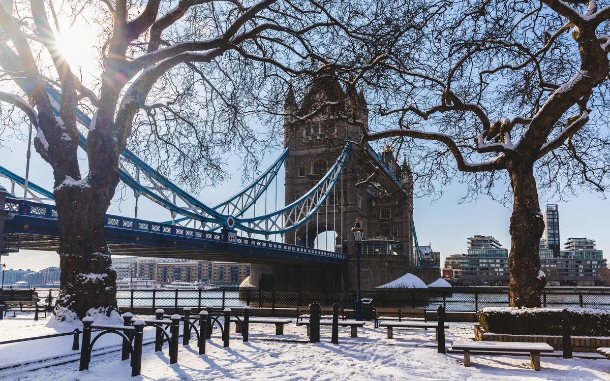 Tower Bridge in London im Winter, umgeben von schneebedeckten Bäumen und Boden.