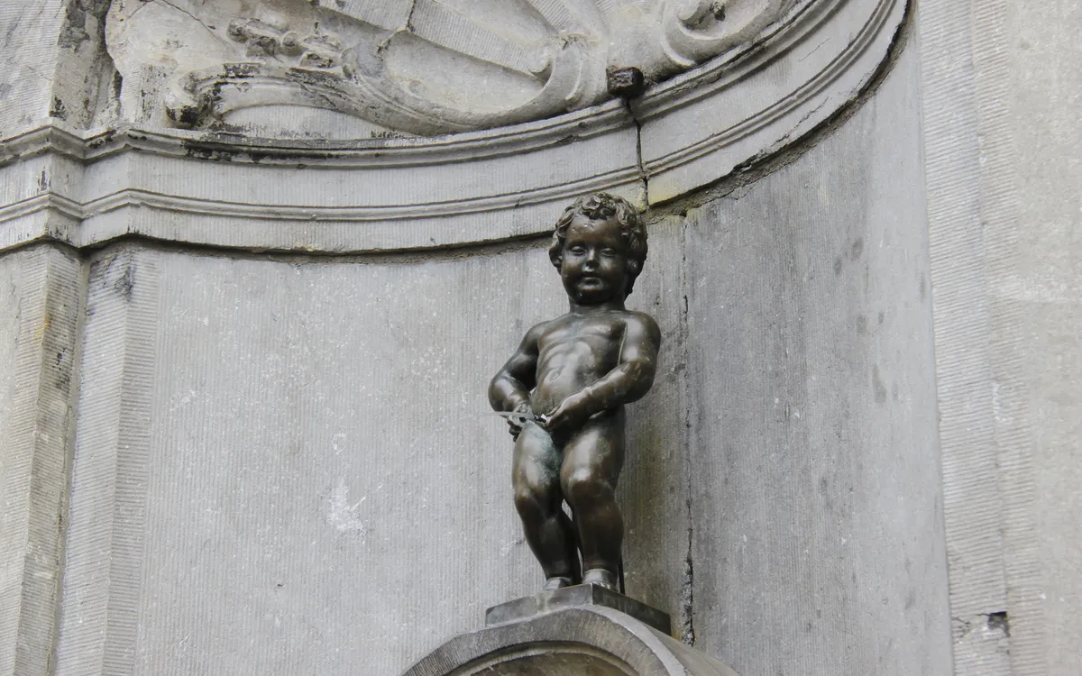Bronzestatue eines kleinen Jungen an einer steinernen Fassade.