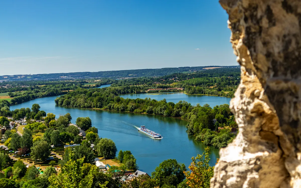 Blick auf einen Fluss mit einem Ausflugsschiff und angrenzender grüner Landschaft.