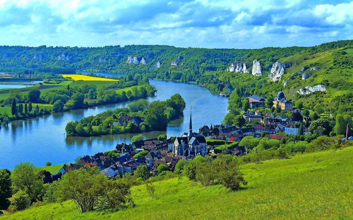Landschaft mit Fluss, Hügeln und Dorf im Vordergrund.