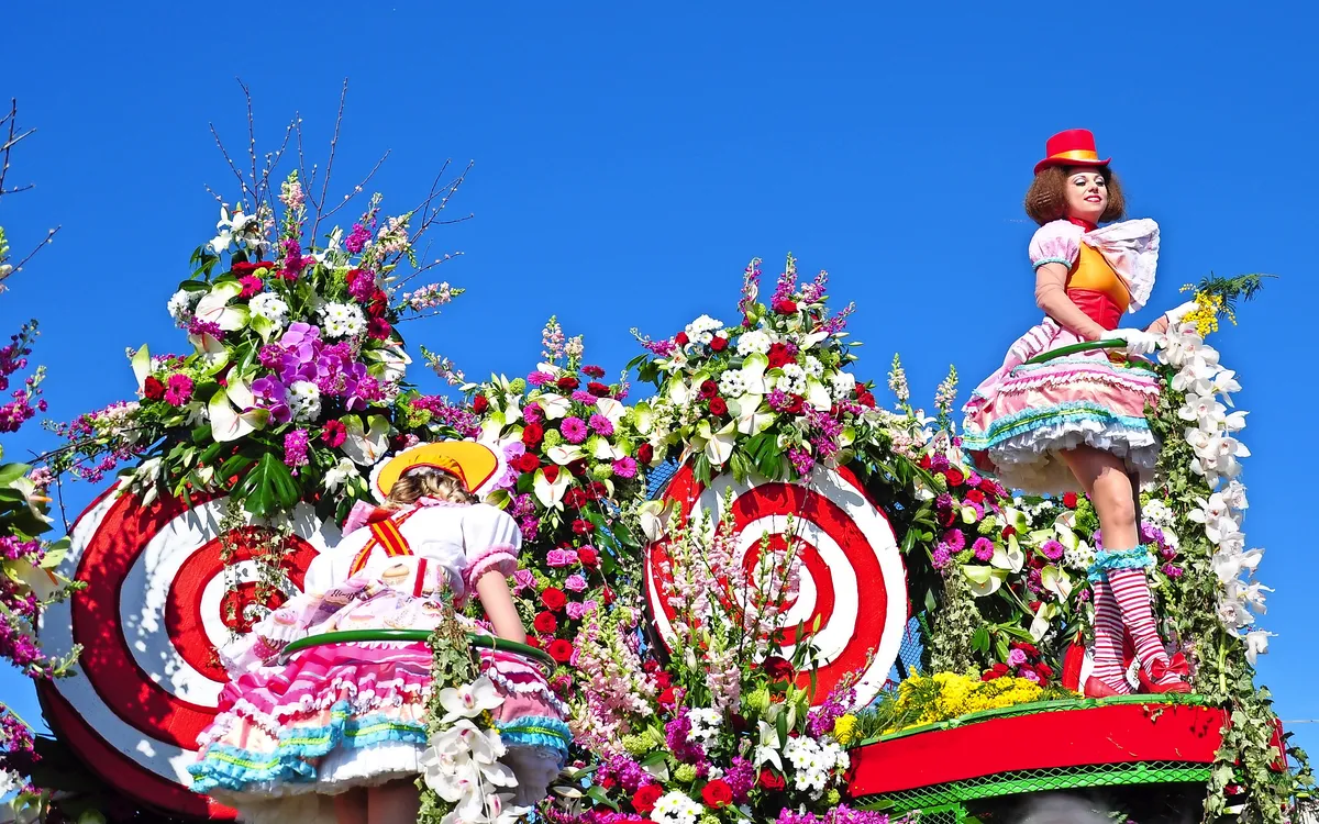Farbenfrohe Parade mit Teilnehmern in blumigen Kostümen und blauem Himmel.