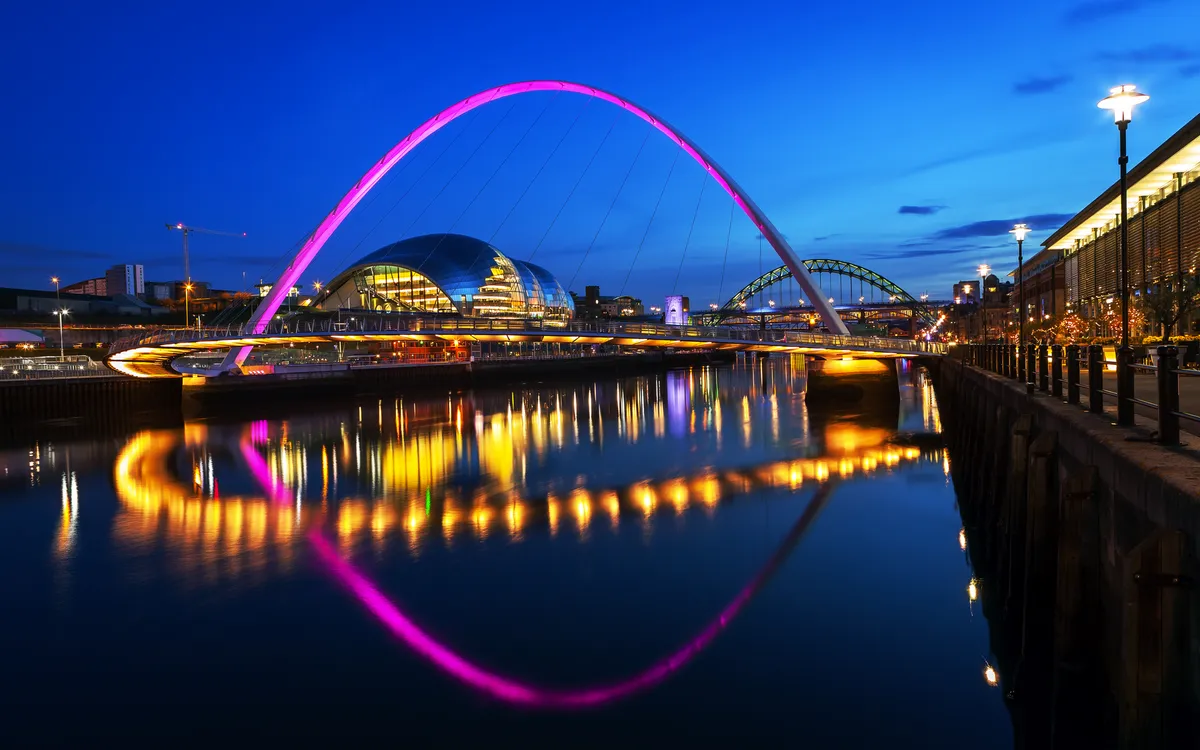 Flusslandschaft mit beleuchteter Brücke und Stadt bei Nacht.