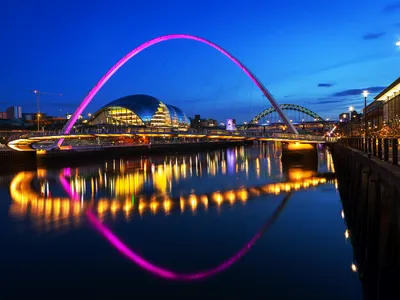 Flusslandschaft mit beleuchteter Brücke und Stadt bei Nacht.