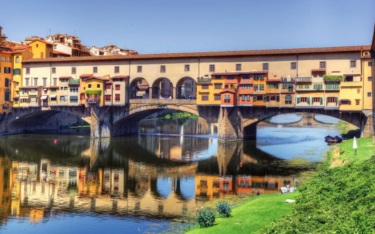 Brücke Ponte Vecchio in Florenz mit bunten Gebäuden, gespiegelt im Fluss Arno.