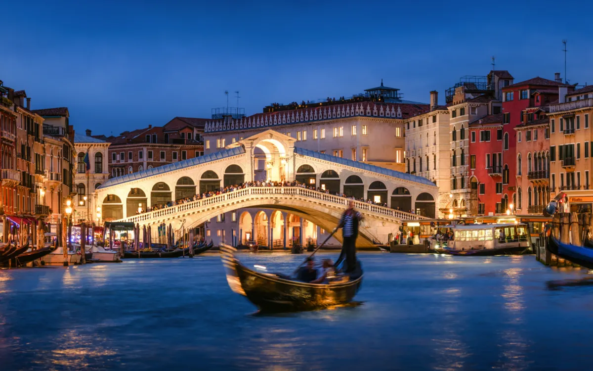 Gondelfahrt bei Nacht auf dem Canal Grande in Venedig mit Blick auf die beleuchtete Rialtobrücke.