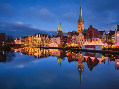 Altstadt mit beleuchtetem Weihnachtsmarkt am Flussufer bei Abenddämmerung.