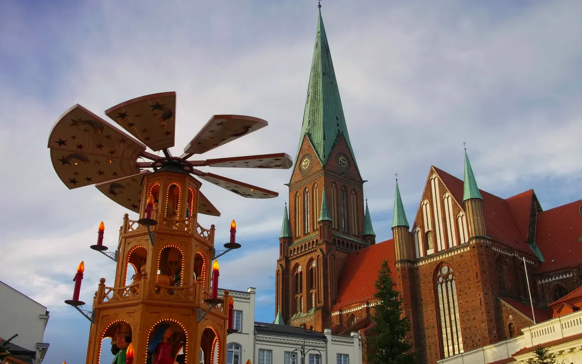 Kirchturm und Weihnachtsmarkt mit Holzpyramide bei Tageslicht.