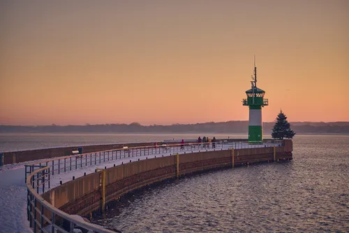 Leuchtturm bei Sonnenuntergang an einem schneebedeckten Steg.