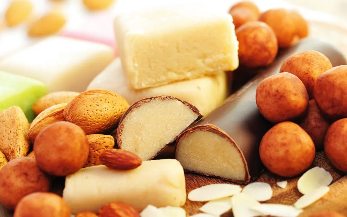 Verschiedene Marzipan-Süßigkeiten und Mandeln auf einem Holzbrett.