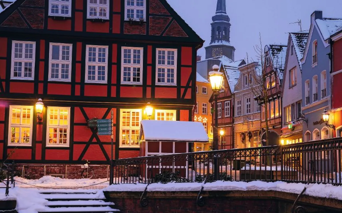 Verschneite Altstadt mit Fachwerkhäusern und Kirchturm im Hintergrund.