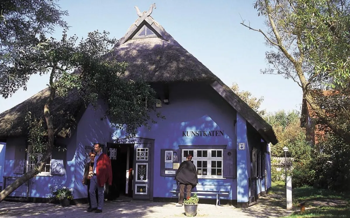 Blaues Reetdachhaus mit Personen vor der Kunstkaten-Galerie in Fischland-Darß-Zingst.