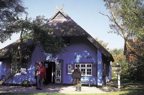 Blaues Reetdachhaus mit Personen vor der Kunstkaten-Galerie in Fischland-Darß-Zingst.