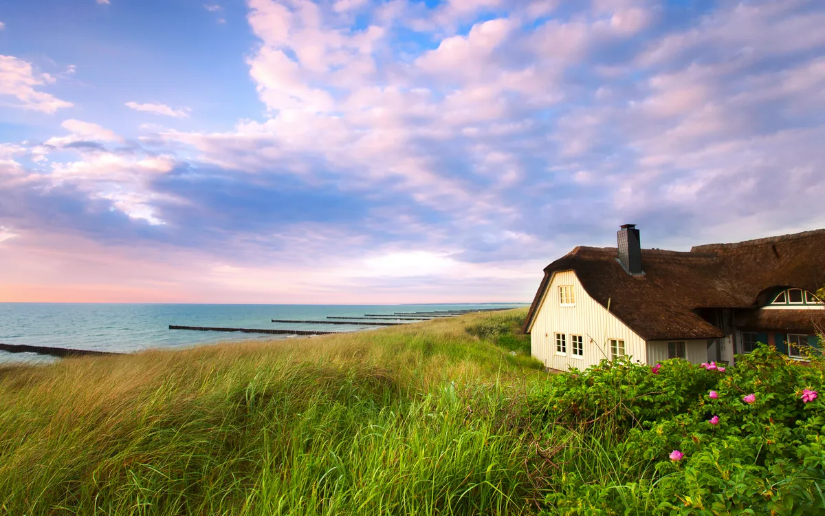 Reetdachhaus an der Ostseeküste in Ahrenshoop, Deutschland, umgeben von Dünen und Meer.