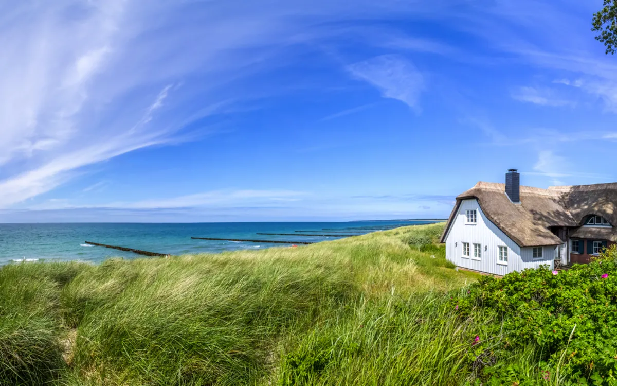 Reetdachhaus an der Ostsee in Ahrenshoop mit Dünen und Meer im Hintergrund