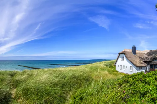 Reetdachhaus an der Ostsee in Ahrenshoop mit Dünen und Meer im Hintergrund