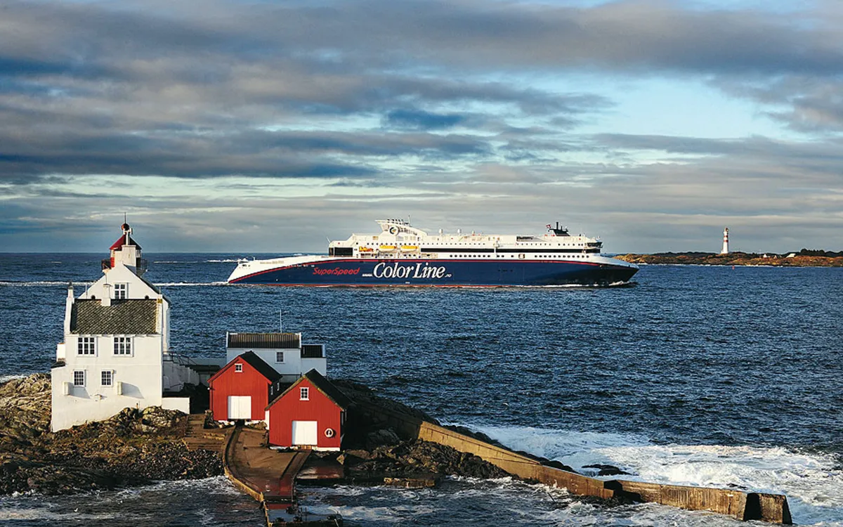 Fähre Color Line auf See, vorne rote und weiße Holzhäuser, hinten ein Leuchtturm.