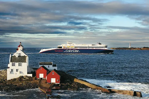 Fähre Color Line auf See, vorne rote und weiße Holzhäuser, hinten ein Leuchtturm.