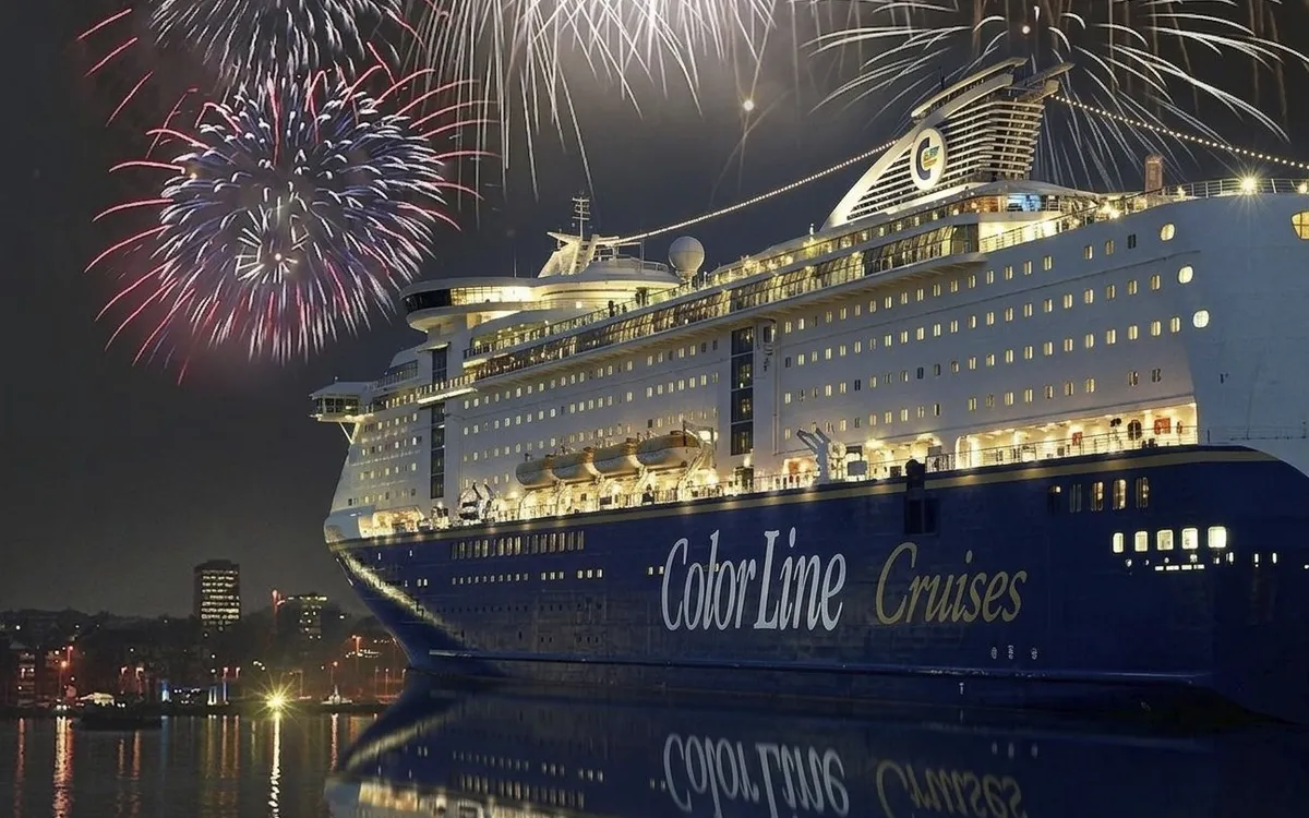 Ein Kreuzfahrtschiff bei Nacht mit Feuerwerk im Hintergrund.