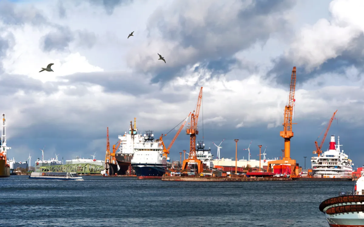 Hafen mit Containerschiffen und Kränen bei bewölktem Himmel.