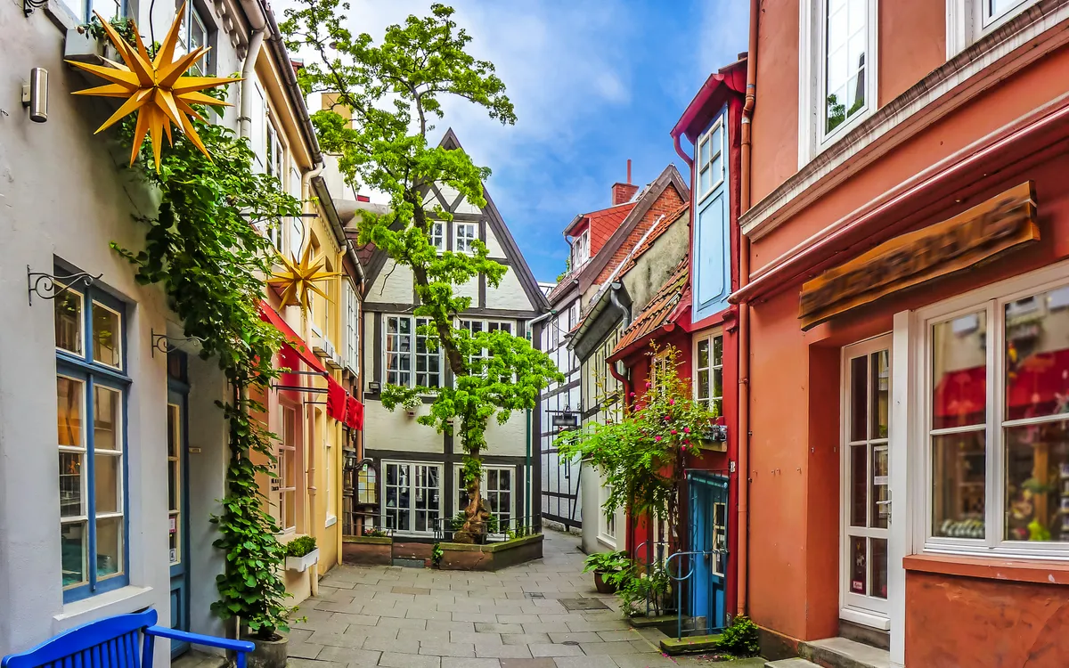 Bunte Fachwerkhäuser in enger, gepflasterter Gasse mit Sternlaterne und blauer Bank.