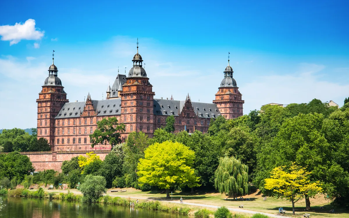 Schloss Johannisburg mit blauem Himmel und grüne Bäume im Vordergrund.