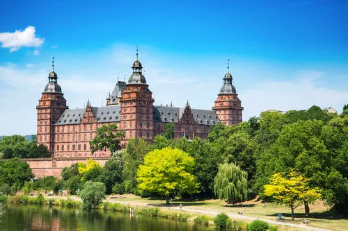 Schloss Johannisburg mit blauem Himmel und grüne Bäume im Vordergrund.