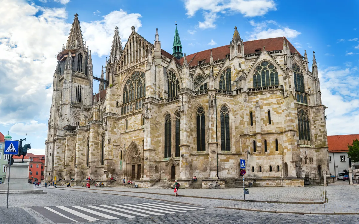 Gotische Kathedrale bei blauem Himmel mit Personen auf einer Kopfsteinpflasterstraße.