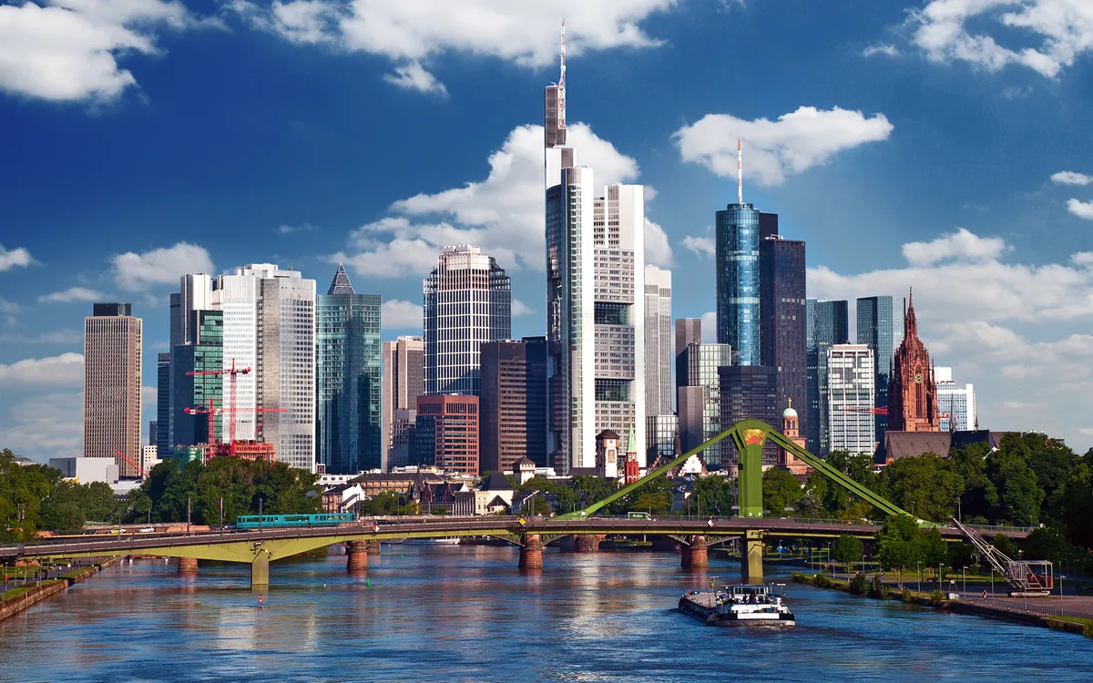 Skyline von Frankfurt am Main mit Wolkenkratzern und Fluss im Vordergrund.