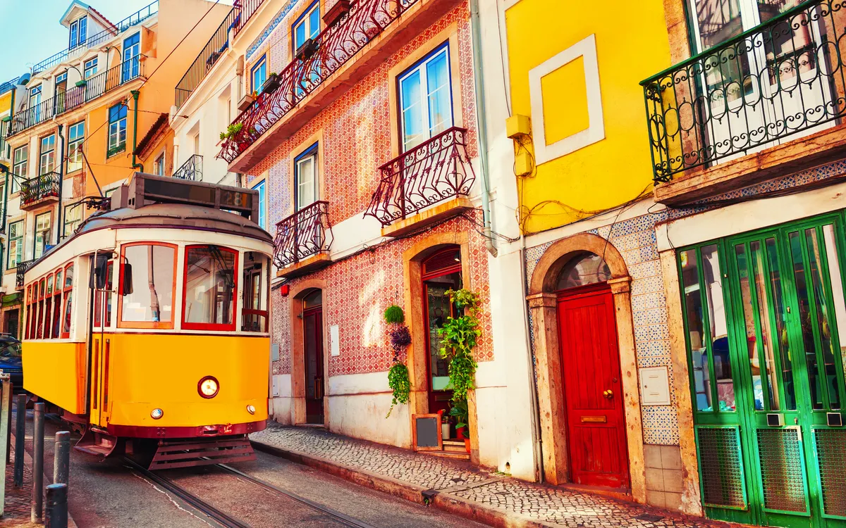 Gelbe Straßenbahn fährt durch enge Straße in Lissabon.