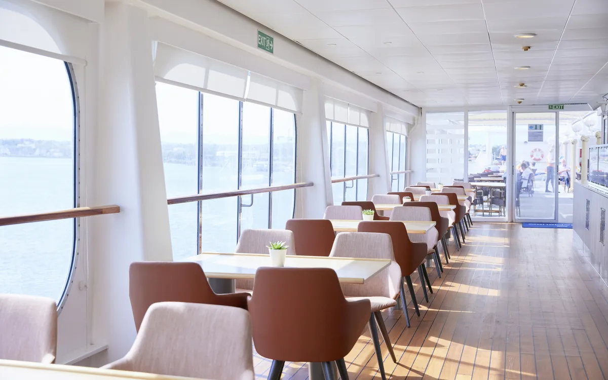 Heller Speiseraum auf einem Schiff mit Tischen und Stühlen, Blick aufs Meer.