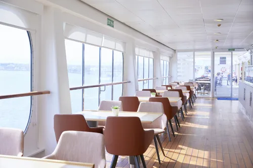 Heller Speiseraum auf einem Schiff mit Tischen und Stühlen, Blick aufs Meer.