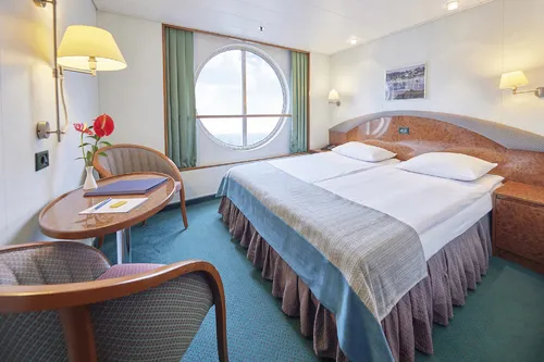 MS Hamburg Außenkabine mit Doppelbett und Sitzbereich, großer runder Fensterblick.