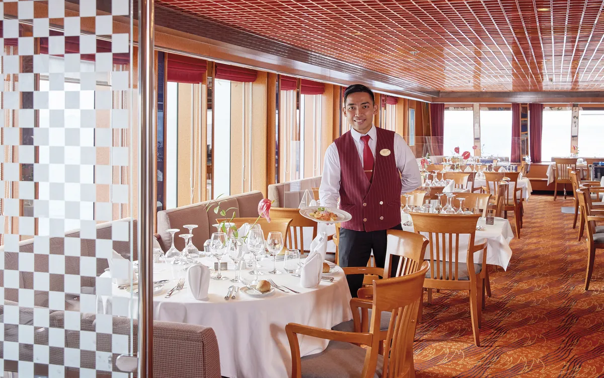 Ein Kellner im MS Hamburg Restaurant neben gedeckten Tischen.