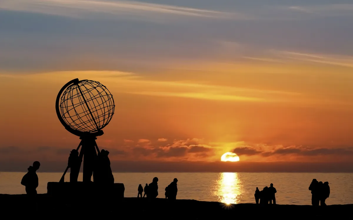Mitternachtssonne am Nordkap mit Globusmonument und Menschen im Abendrot.